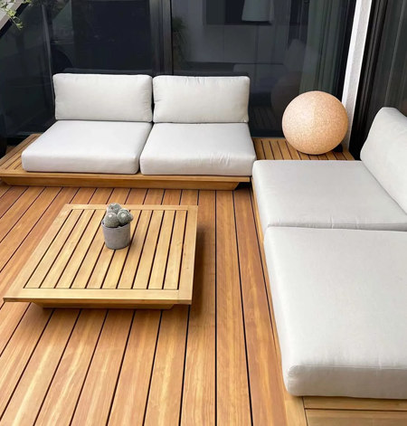 Holzterrasse mit Lounge-Sofa mit hellen Polstern und niedrigem Couchtisch aus Holz